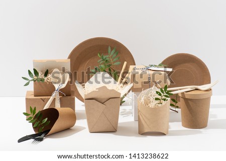 Eco friendly, disposable, recyclable, compostable tableware. Paper food boxes, dishes and flower pots with saw shawings and rowan branches in them and cornstarch cutlery over white background