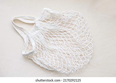 Eco friendly mesh bag on a light wooden background. String bag made of white cotton threads. Zero waste lifestyle.