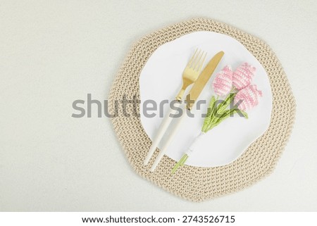 Eco friendly table setting with handmade knitted tulips, gold cutlery and white plate on a crochet placemat. Sustainable celebration decor for allergy free wedding or spring event, top view
