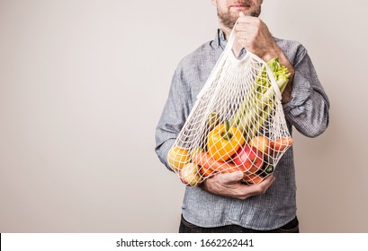 Eco friendly (zero waste) lifestyle and healthy diet concept. Man holding reusable mesh shopping bag with fresh fruits and vegetables. Neutral background with free copy (text) space. - Powered by Shutterstock