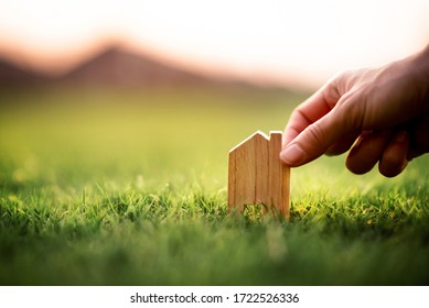 Eco House Concept, Hand Holding Small Model Of Home Over Green Grass.