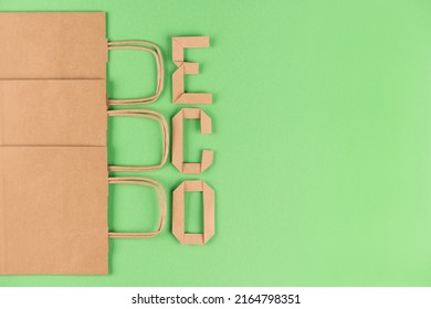 Eco Kraft Paper Recycled Bags With Paper Letters Word ECO Over Green Background With Copy Space. Street Food Take Away Or Shopping Paper Bag, Sustainable Packaging Concept. Ethical Consumerism