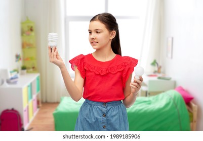 Eco Living And Sustainability Concept - Smiling Girl Comparing Energy Saving Light Bulb With Incandescent Lamp Over Kids Room Background