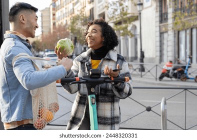 An eco-friendly couple laughing and making jokes on the street. She rides an electric scooter and he recycles bags. - Powered by Shutterstock