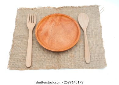 Eco-friendly dining set with an empty wooden plate, fork, and spoon on a natural burlap cloth, emphasizing sustainable tableware.
