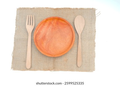Eco-friendly dining set with an empty wooden plate, fork, and spoon on a natural burlap cloth, emphasizing sustainable tableware.