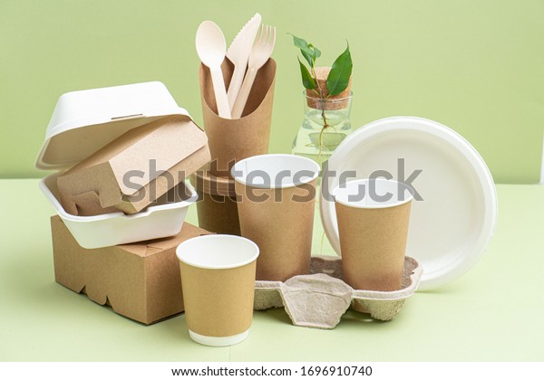 Eco-friendly disposable bamboo\
cutlery, paper and sugarcane containers for food and drinks over\
green background. Side view on composition. Plant branch in bottle\
behind.