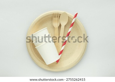 Eco-friendly disposable tableware set with biodegradable plate, wooden fork and spoon, paper cups, and striped paper straw on minimal background. Concept of sustainability, zero waste lifestyle, and plastic free food packaging.