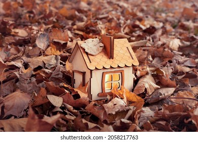 Eco-friendly Home. Wooden House With Fallen Autumn Leaves. Model Of A Wooden House In The Forest, Cozy Light From The Window, A Dream For A Happy Family Life