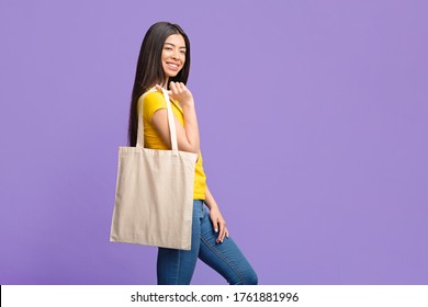 Eco-Friendly Lifestyle. Cheerful Asian Girl Posing With Blank Tote Eco Bag Over Purple Studio Background, Copy Space