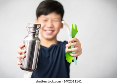 Eco-friendly lifestyle concept. Smart looking Asian teen boy smiling and stretching his arms forward holding Reusable stainless bottle, green spoon and fork, and colorful silicone straw.  Zero waste.