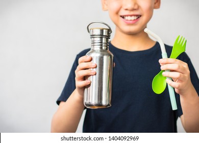 Eco-friendly lifestyle concept. Smart looking Asian boy smiling and holding stainless bottle, reusable green spoon and fork, and colorful silicone straw. Stop plastic waste
