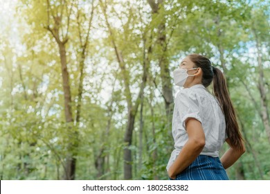 Máscara facial sostenible ecológica. Mujer con máscaras coreanas kn95 caminando en un bosque al aire libre mirando hacia el sol. Concepto de esperanza para el medio ambiente. Cubierta de coronavirus.