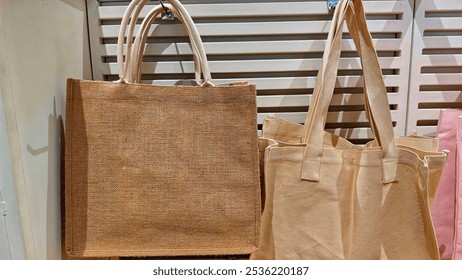 Eco-friendly tote bags made from jute and cotton materials, hanging on display. The natural, reusable bags are ideal for sustainable shopping and environmentally conscious consumers. - Powered by Shutterstock