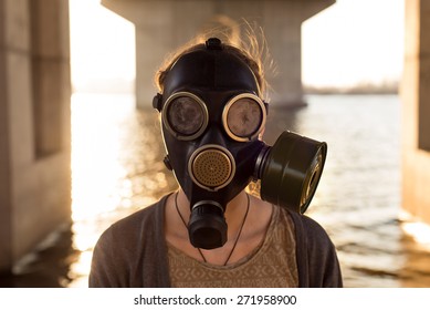 Ecological concept of air contamination. Portrait of woman in gas mask near water