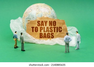 Ecological concept. On a green background on a plastic bag is a globe and a sign with the inscription - SAY NO TO PLASTIC BAGS. Near out of focus figures of people