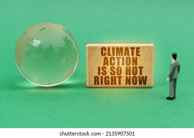 Ecological Concept. On The Green Surface Is A Globe And A Figurine Of A Man Who Looks At A Sign With The Inscription - Climate Action Is So Hot Right Now