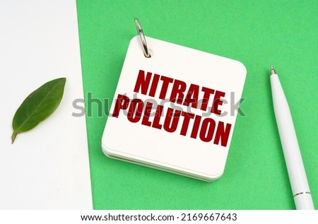 Ecological concept. On a white-green surface, a piece of paper, a pen and a notepad with the text - nitrate pollution