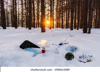 Ecological crisis. Different garbage and trash on snow at beautiful winter forest at bright sunrise with sunbeams through trees. Environmental pollution by garbage. Destructive human influence on