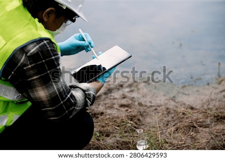 Ecologist observing water quality with flask and tablet by the water's edge in a natural environment