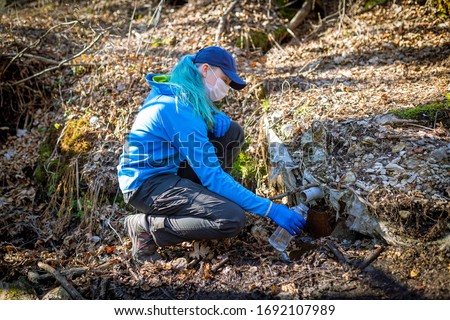 Ecologist taking water samples from a natural source in protective gloves