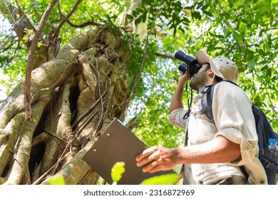 Ecologist,national park,forester,environmental conservation concept.man park ranger in uniform looks through binoculars and monitoring the forest area in summer or autum.  - Powered by Shutterstock