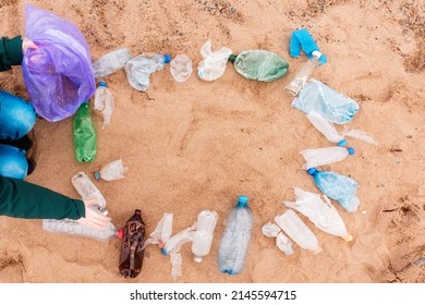 Ecology Template. Volunteer Picking Up A Garbage. Frame From Plastic Dirty Bottles With Copy Space On A Sandy Beach. Top View. The Concept Of Environmental Protection And Earth Day.