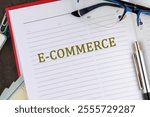 E-COMMERCE - activity of electronically buying or selling of products on online services. E-COMMERCE word it is written in the business book in close-up, top view.