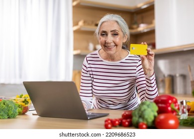 E-Commerce Concept. Smiling Senior Woman With Laptop Computer And Credit Card Posing In Kitchen Interior, Happy Elderly Lady Enjoying Online Payments And Internet Shopping, Copy Space