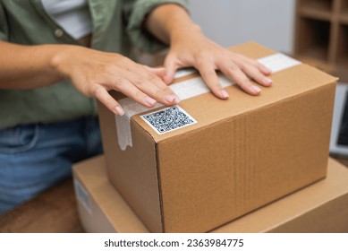 E-commerce at its core: Woman's hands apply a QR code sticker to a package, symbolizing online shopping and shipping.  - Powered by Shutterstock