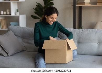 Ecommerce. Satisfied Young Latin Woman Web Shop Customer Sit On Sofa Open Postal Delivery Package With Consumer Goods Products Ordered Online. Happy Millennial Lady Unpacking After Moving To New Home