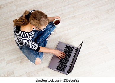 E-Commerce-Frau. Junge Frau, die Computer zum Online-Shopping nutzt, auf dem Boden sitzt und Kaffee trinkt.
