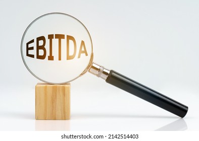 Economic concept. On a white surface there is a cube and a magnifying glass inside which is the inscription - EBITDA