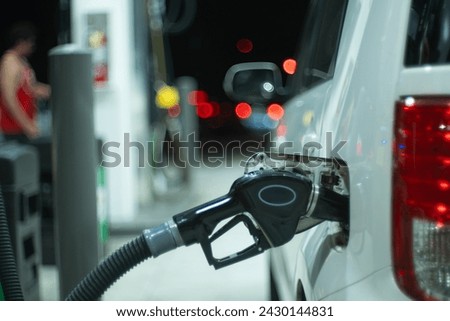 Economy car at gas station being filled up with regular gasoline fuel at night. Closeup, shallow DOF.