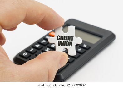 Economy And Finance Concept. A Man Holds In His Hands A Puzzle With The Inscription - Credit Union. In The Background Is A Calculator.