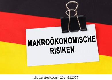 Economy and finance concept. On the flag of Germany lies a business card with the inscription - macroeconomic risks. Text in German. - Shutterstock ID 2364812577