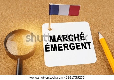 Economy and finance concept. On the table are a magnifying glass, a pencil, the flag of France and a sheet of paper with the inscription - emerging market. Text in French.