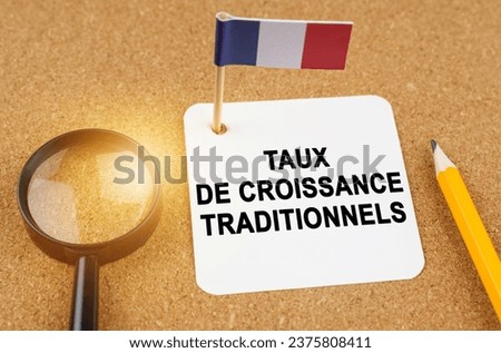 Economy and finance concept. On the table are a magnifying glass, a pencil, the flag of France and a sheet of paper with the inscription - traditional growth rates. Text in French.