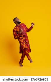Ecstatic black man in traditional african clothes dancing over yellow studio background