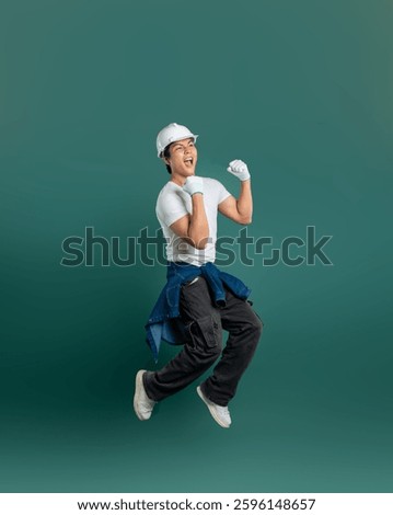 Ecstatic construction worker jumping for joy in work attire against a solid background, celebrating a job well done!