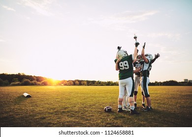 Ecstatic Group Of American Football Players Standing In A Huddle And Raising A Championship Trophy In Celebration