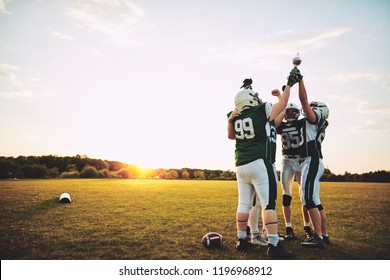 Ecstatic Group Of American Football Players Standing In A Huddle And Celebrating With A Trophy After A Championship Games