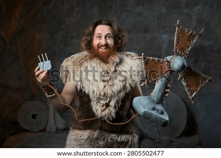An ecstatic prehistoric man with a red beard and fur clothing holds a primitive stone fan and its electric plug. His joyful and surprised expression humorously suggests he has finally found a way to make his ancient appliance work, parodying modern satisfaction with technology and utility services.
