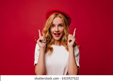 Ecstatic white girl in beret posing with amazement. Elegant caucasian female model in t-shirt standing on red background. - Shutterstock ID 1415927522