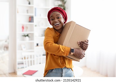 Ecstatic young african american muslim woman in casual embracing box with something and smiling, home interior, making order on Internet with delivery, copy space. Delivery service, shipment concept