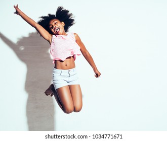 Ecstatic young African girl with long curly hair shouting and jumping in the air with her arm raised against a white background