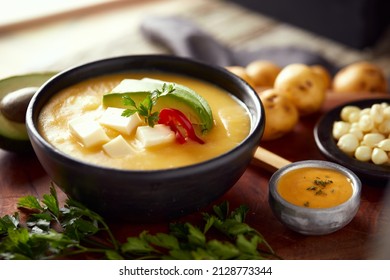 Ecuadorian locro de papa a traditional potato and cheese soup served with avocado and hominy. It’s on a wooden background - Shutterstock ID 2128773344