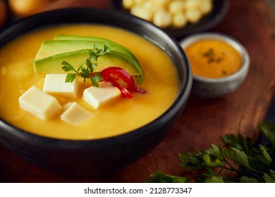 Ecuadorian locro de papa a traditional potato and cheese soup served with avocado and hominy. It’s on a wooden background - Shutterstock ID 2128773347
