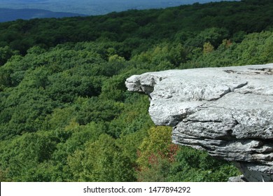 Edge of cliff view from the left with forest in the background and mountain ranges in the distance