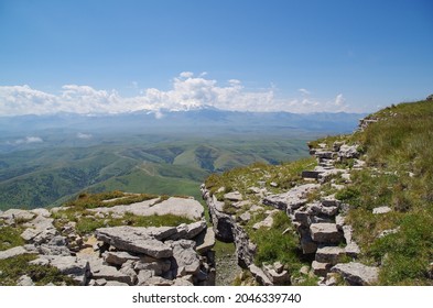 At the edge of crevice. Beautiful view of green valley, snowy Mount Elbrus and mountain chains of Greater Caucasus from Malyy Bermamyt Plateau. Nature and travel. Russia, Caucasus, Karachay-Cherkessia
